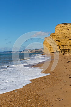 UK Jurassic coast Burton Bradstock beach Dorset with sandstone cliffs and white waves in summer with blue sea and sky