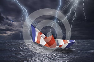 UK paper boat made as the flag of the United Kingdom almost capsizes in high waves. Bolt of lightning