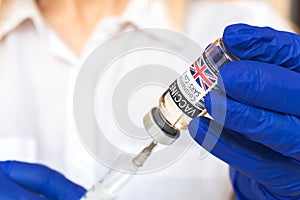 UK vaccine vial in doctor hands, injection by a syringe needle close-up shot, vaccination and healthcare concept