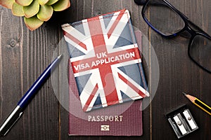 Uk visa application concept: a union jack colored wallet over a generic passport on a wooden desktop