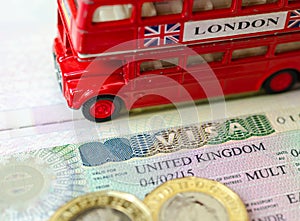UK visa sticker in a passport surrounded by pound coins and double-decker bus model. Concept for travel and holiday