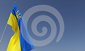 Ukraine flag on flagpole on blue background. Place for text. The flag of Ukraine with coat of arms is unfurling in the wind. Kyiv
