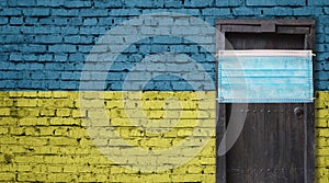 Ukraine flag painted on brick wall and closed door with medical mask protected