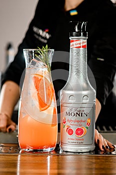 UKRAINE, KYIV - MARCH 11, 2021: Close-up of bottle of Ruby Grapefruit Syrup by Monin and glass carafe of iced cocktail