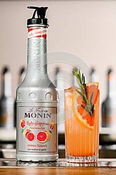 UKRAINE, KYIV - MARCH 11, 2021: Close-up of bottle of Ruby Grapefruit Syrup by Monin and glass of cocktail with citrus