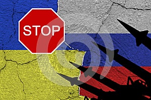 Ukraine and russia flags on old cracked wall with antiaircraft rockets silhouettes and sign `STOP`