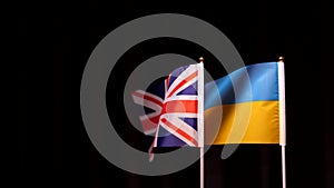 Ukraine and UK flags waving slowly against dark curtain