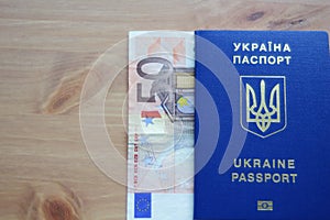 Ukrainian biometric passport with fifty euros banknote on wooden table.