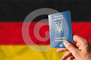 Ukrainian biometric passport in the hand of a person against the background of the national flag of Germany. Citizenship of