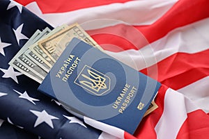 Ukrainian biometrical passport and US dollar bills on folded waving flag of United States of America