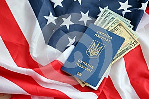 Ukrainian biometrical passport and US dollar bills on folded waving flag of United States of America