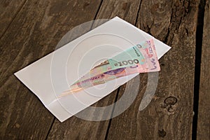 Ukrainian cash currency lies in a white envelope on an old wooden table, salary in an envelope