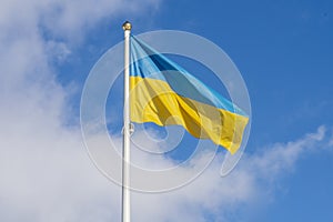The Ukrainian flag on the flagpole is fluttering in the wind against a blue sky with clouds. Concept: Ukrainians` struggle for ind