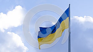 The Ukrainian flag on the flagpole flutters against the background of a blue sky with clouds. Concept: Ukrainians` struggle for in