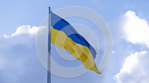 The Ukrainian flag on the flagpole flutters against the background of a blue sky with clouds. Concept: Ukrainians` struggle for in