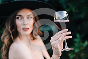 Ukrainian girl in a black dress outdoors in a hat with a glass of red wine
