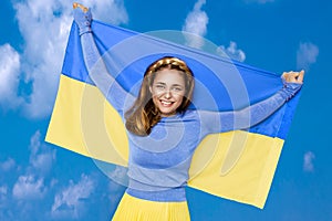 Ukrainian girl carries blue and yellow flag of Ukraine fluttering on the blue sky background.