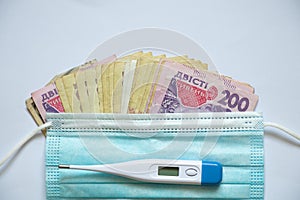 ukrainian hryvnia electronic thermometer and medical mask on a white background, finance and medicine, money health