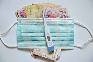 ukrainian hryvnia electronic thermometer and medical mask on a white background, finance and medicine, money health