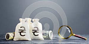 Ukrainian hryvnia money bags and magnifying glass. Financial monitoring of suspicious cash transactions. Search sources of