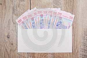 Ukrainian hryvnias in a white envelope on a wooden background. Banknotes of 200 hryvnia. Financial concept.