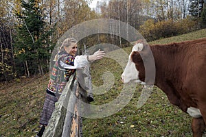 Ukrainian hutsul woman in national costume standing near the fence and caresses the cow