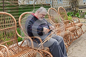 Ukrainian man cut sleeving while making whicker rocking chair in summer garden