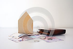 Ukrainian money, coins, brown leather wallet and carton house stands on the white table.