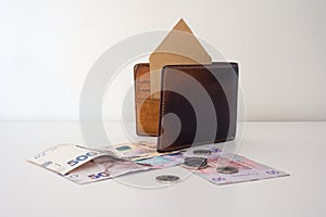 Ukrainian money, coins, brown leather wallet and paper house stands in it.
