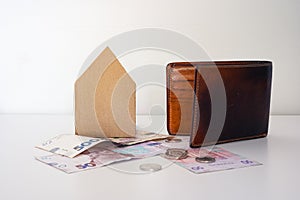 Ukrainian money, coins, brown leather wallet and paper house stands on the white table.