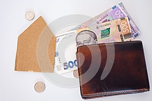 Ukrainian money, coins, brown leather wallet and paper house on the white background.