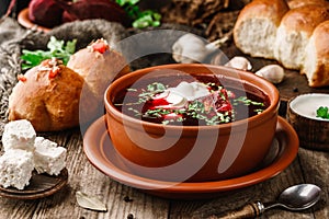 Ukrainian and Russian traditional beet root soup or borscht in bowl with rib eye meat, sour cream, buns, goat cheese, garlic,