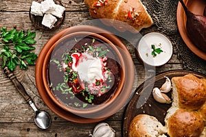 Ukrainian and Russian traditional beet root soup or borscht in bowl with rib eye meat, sour cream, buns, goat cheese, garlic,