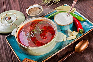 Ukrainian and Russian traditional beetroot soup - borscht in bowl with sour cream, garlic, herbs and bread on wooden background