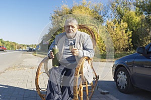 ukrainian senior man sitting in rrocking chair on roadside and holding vacuum bottle