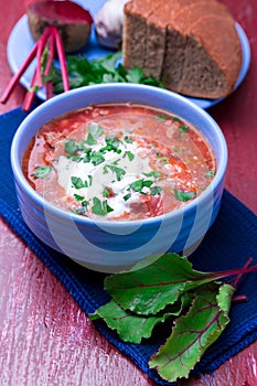 Ukrainian traditional borsch. Russian vegetarian red soup in blue bowl on red wooden background. Borscht, borshch with beet. Clo