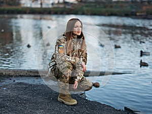Ukrainian woman soldier resting in park during her vacation and watching for ducks in lake