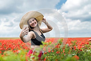 Ukrainian woman in sportswear and straw hat taking a photo selfie with smartphone in poppies field