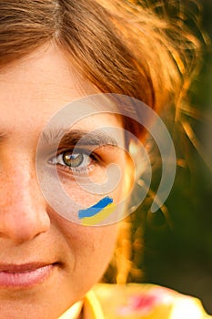 Ukrainian woman. Ukrainian flag on the cheeks. Portrait of a young woman 20, 25 years old. Half face, one green eye