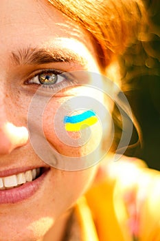 Ukrainian woman. Ukrainian flag on the cheeks. Selfie of a young woman 20, 25 years old. Half face, one green eye, brown hair.