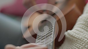 Ukulele in female hands. A woman learns to play the ukulele at home while sitting on the couch.