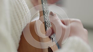 Ukulele in female hands. A woman learns to play the ukulele at home while sitting on the couch.