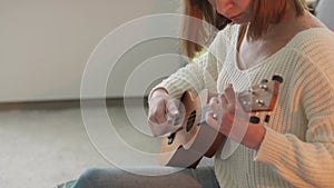 Ukulele in female hands. A woman learns to play the ukulele at home while sitting on the couch.