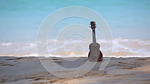 An ukulele, hawai instrument put on the beach and blue sea and wave