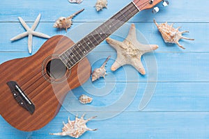 Ukulele and sea shell on light blue wood plank floor for summer