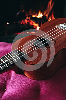 Ukulele small guitar close up stings, fireplace on the background. Musical concept, guitar fret board macro, fire in chimney, cos