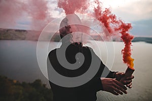 Ultras hooligan holding red smoke bomb in hand, standing on top of rock mountain with amazing view on river. Atmospheric moment.