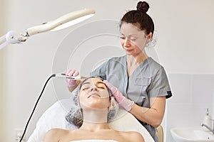 Ultrasonic cleaning of face. Young girl has ultrasound peeling. Cosmetologist makes procedure for skin rejuvenation via modern