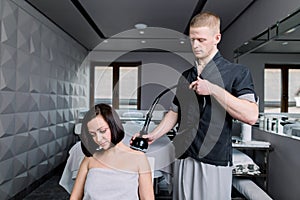 Ultrasound cavitation body treatment. Young brunette woman getting vibro massage therapy in beauty salon. Young man