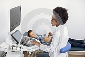 Ultrasound examination of the child in modern clinic. Young afro american female confident doctor makes an abdominal
